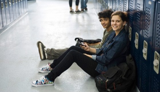 High school student sitting on floor with friend by lockers in school corridor